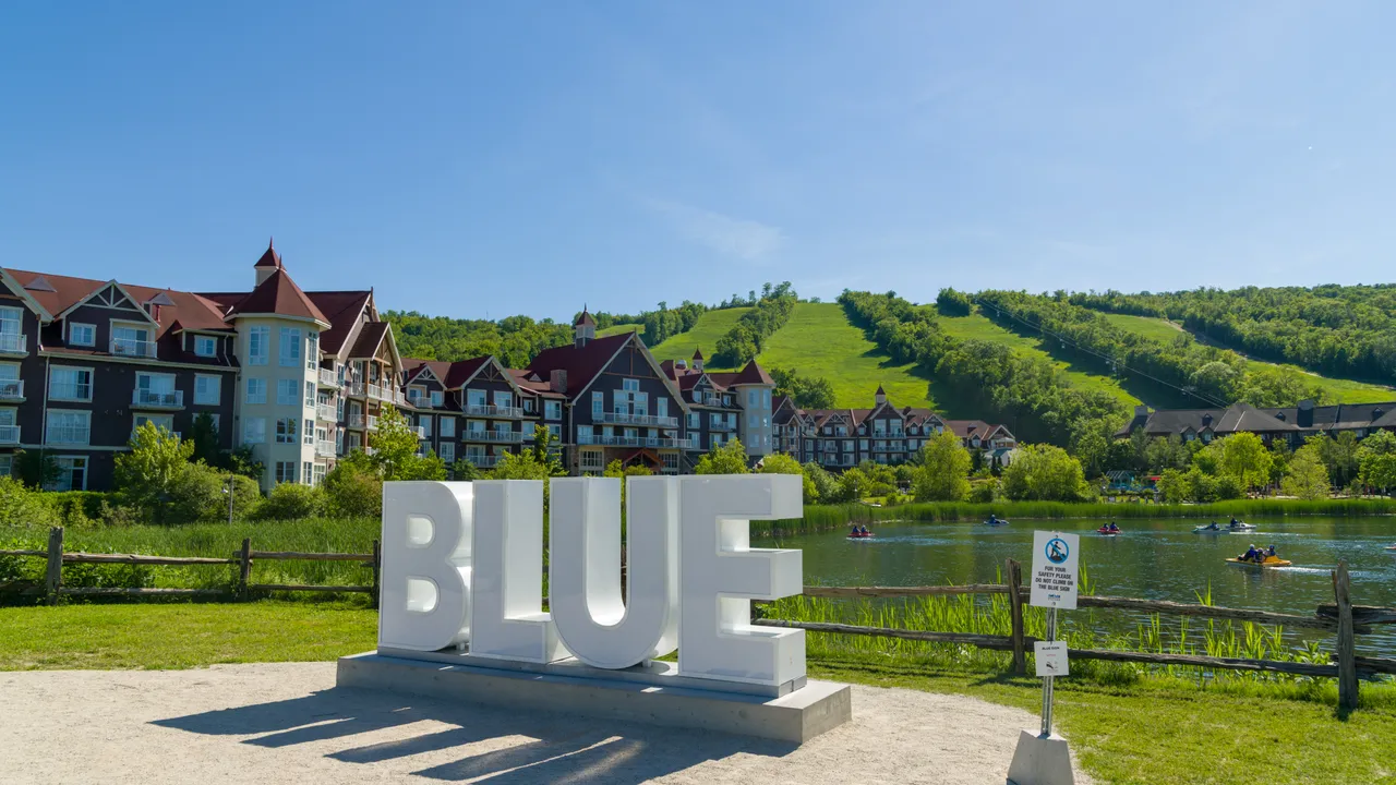 Blue Mountain Village and its green ski hills in summer, beside the pond and the BLUE sign.