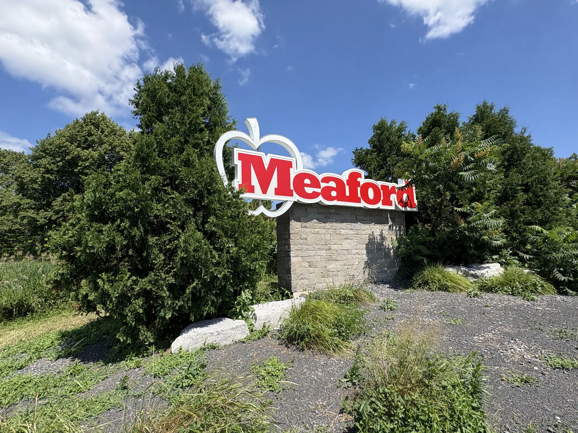 The red apple-logo Meaford welcome sign among cedar trees at the edge of town