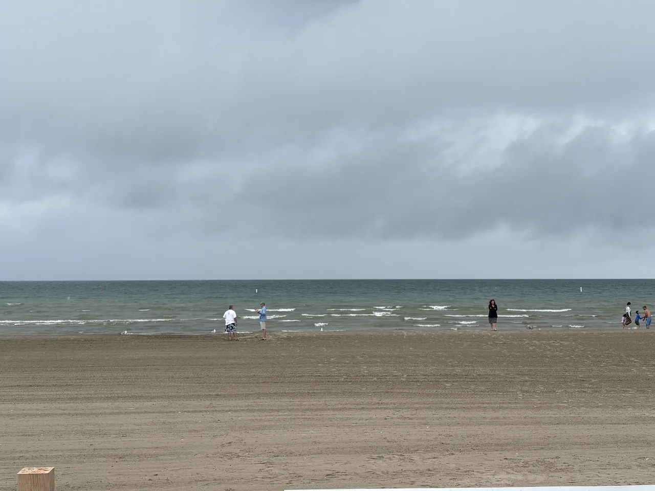 Visitors walking the Nottawasaga Bay shoreline at Wasaga Beach on a grey summer day.