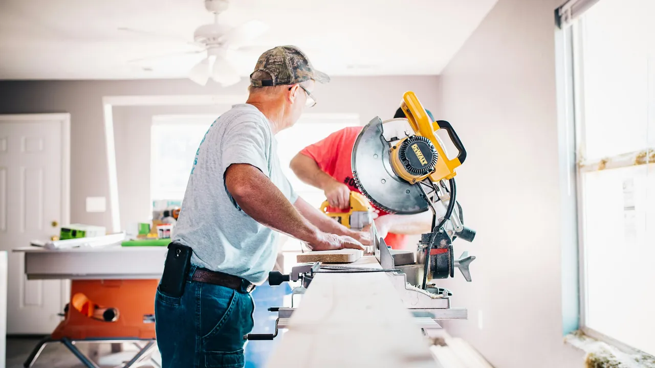 Two tradesmen cutting trim with a mitre saw inside a house under renovation.