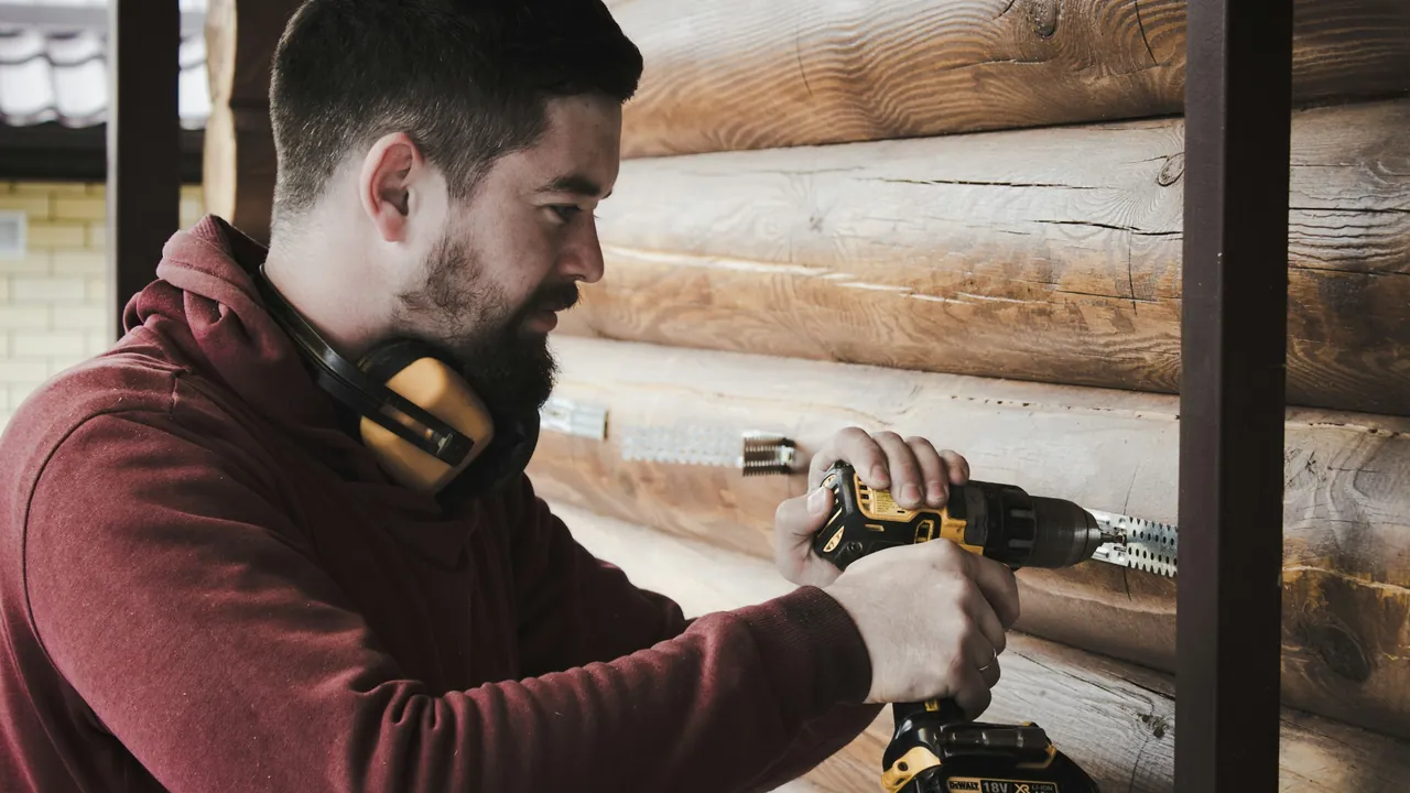 A contractor driving screws into the log wall of a cabin.