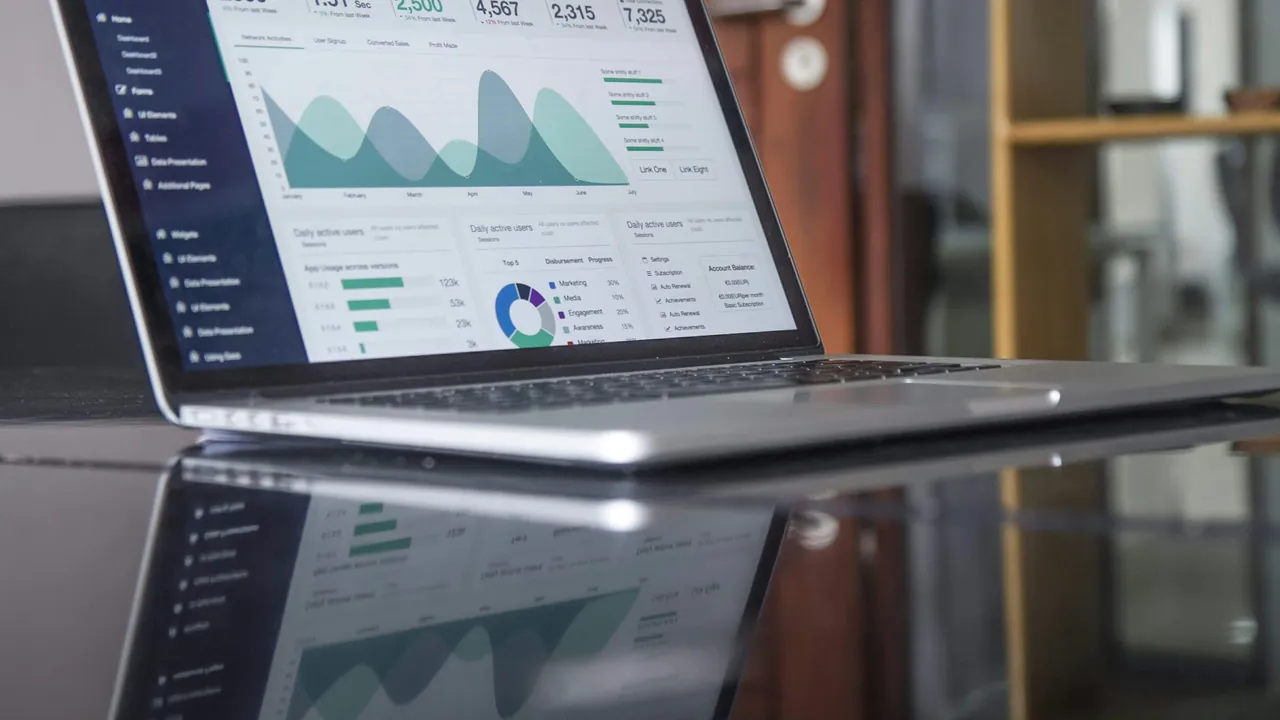 A laptop on a desk shows an analytics dashboard with line charts and summary figures in a bright room.