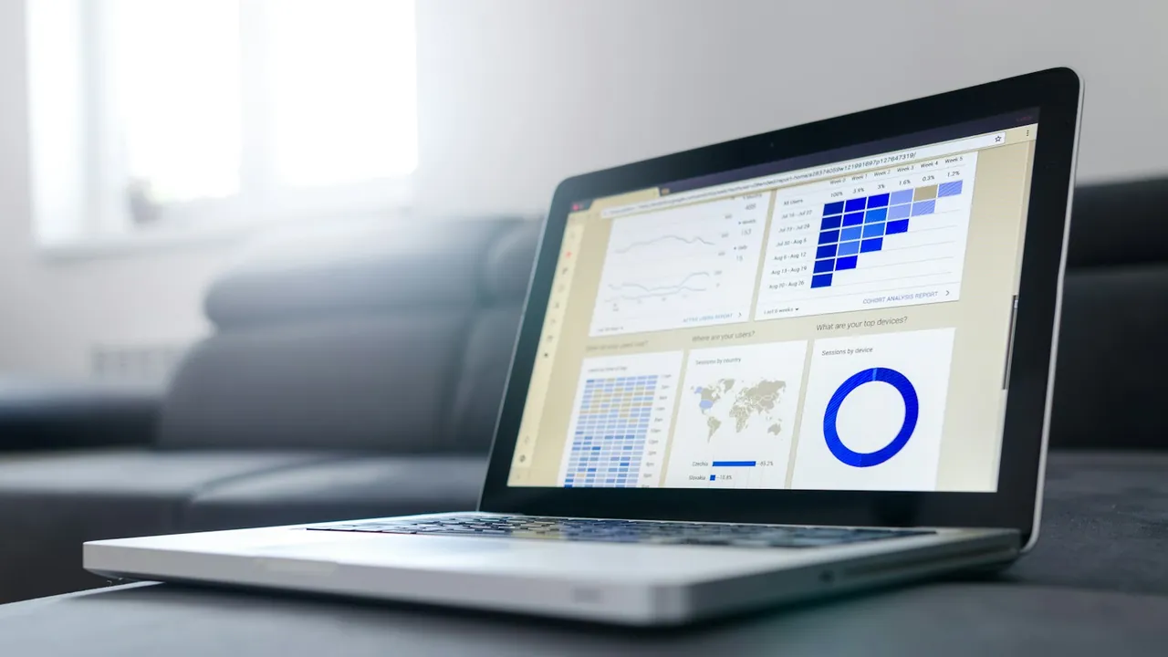 Open laptop on a grey sofa showing a reporting dashboard with a heat map table, a world map and a ring chart.