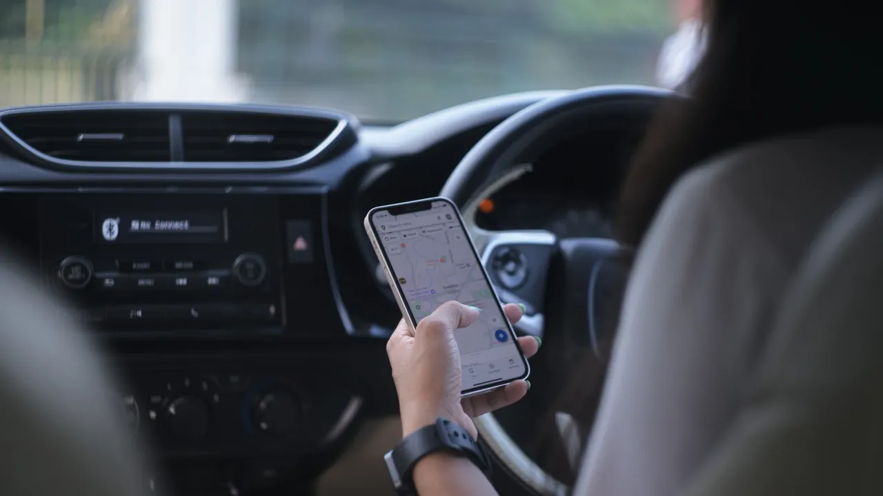 A driver holding a phone with Google Maps open in a car.