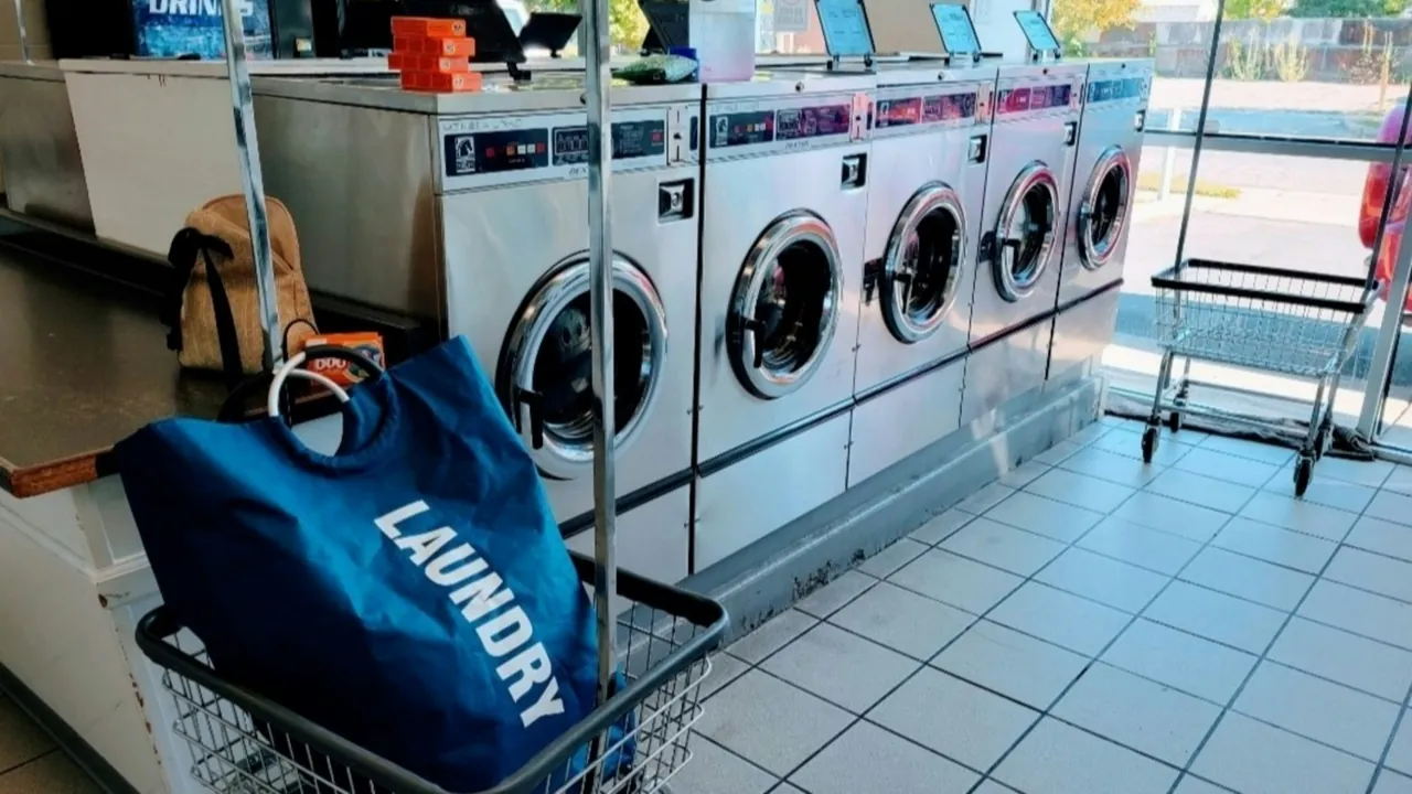 A laundry bag in a cart in front of a row of laundromat washers.