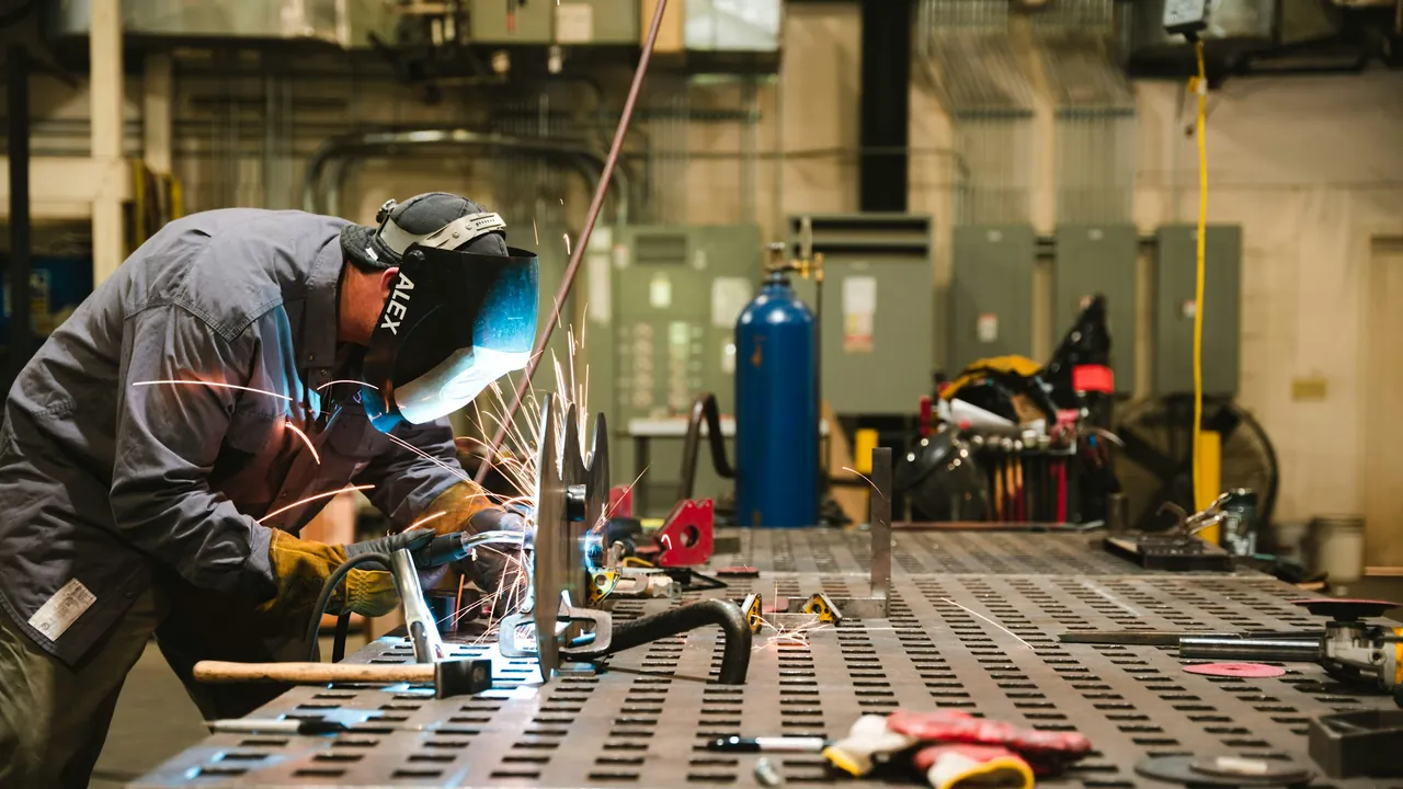 A welder joining steel at a workbench in a fabrication shop.