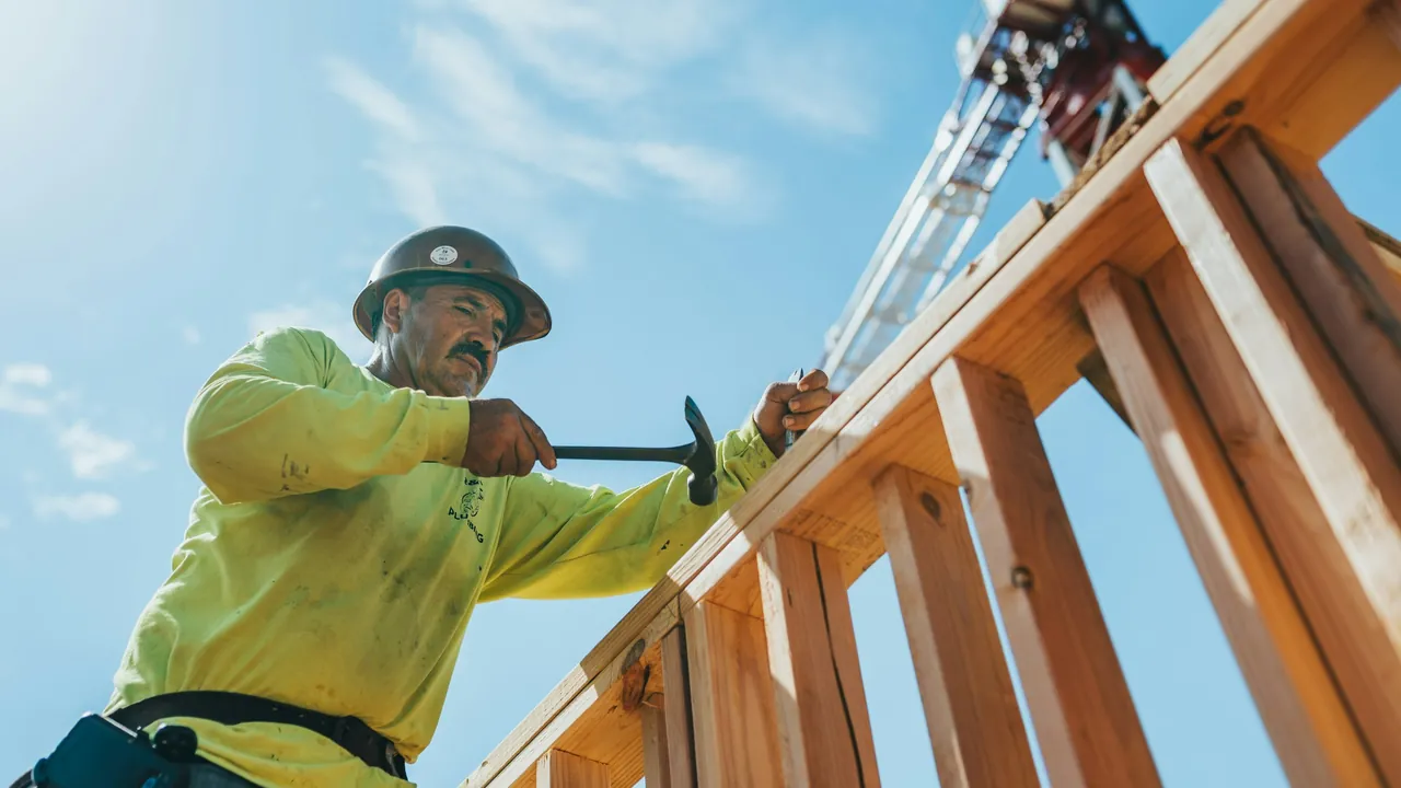 A carpenter framing a timber wall against a blue sky.
