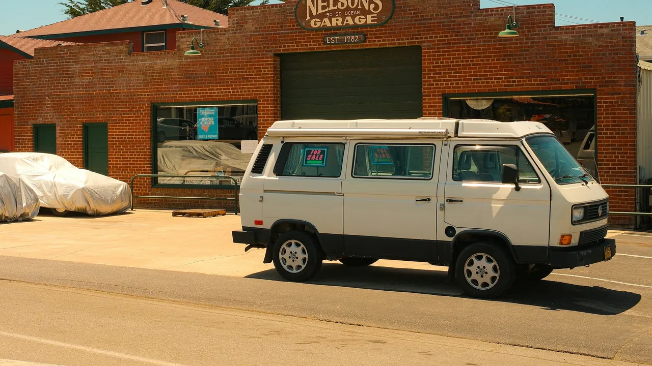 A camper van parked outside a brick garage with the business name above the door.