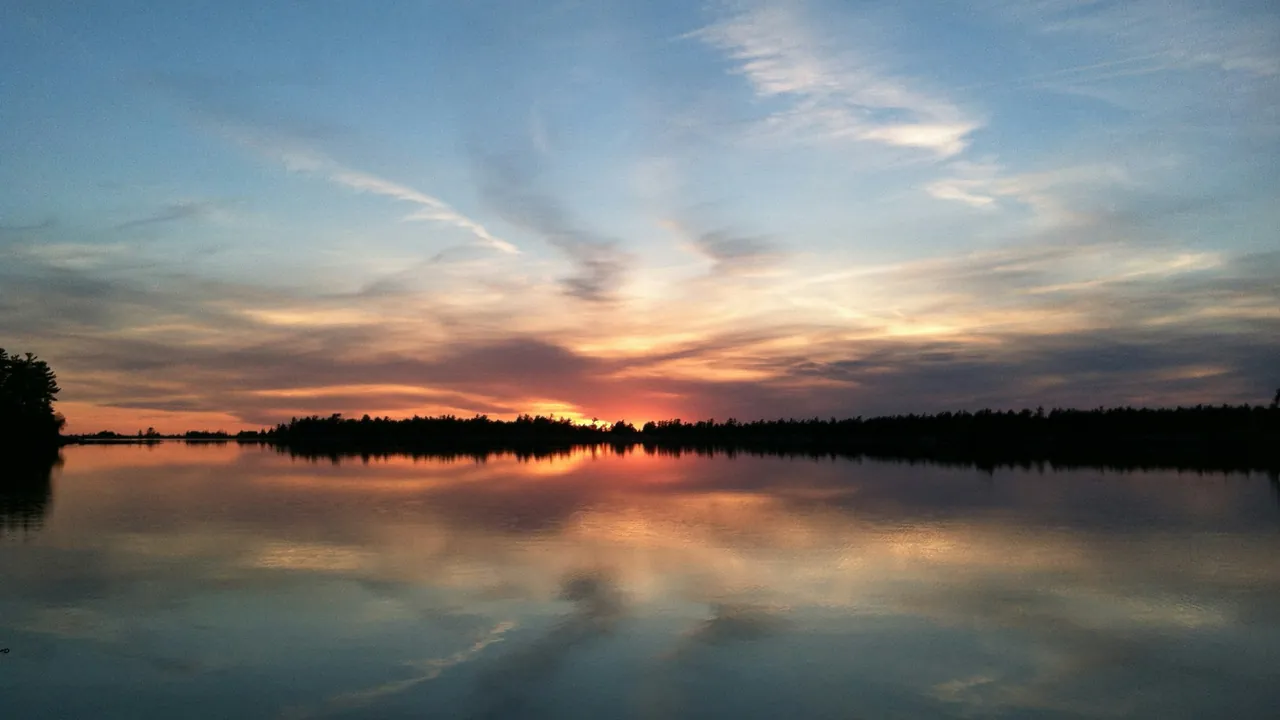 A sunset over the calm water of Georgian Bay, with a tree-lined shore on the horizon.