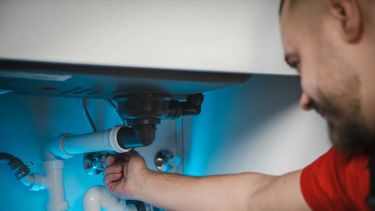 A plumber repairing the pipes under a sink.