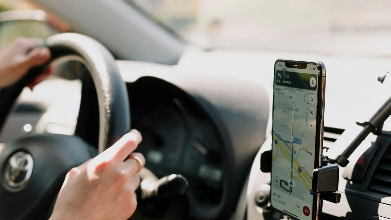 A phone in a dashboard mount showing Google Maps directions while someone drives.